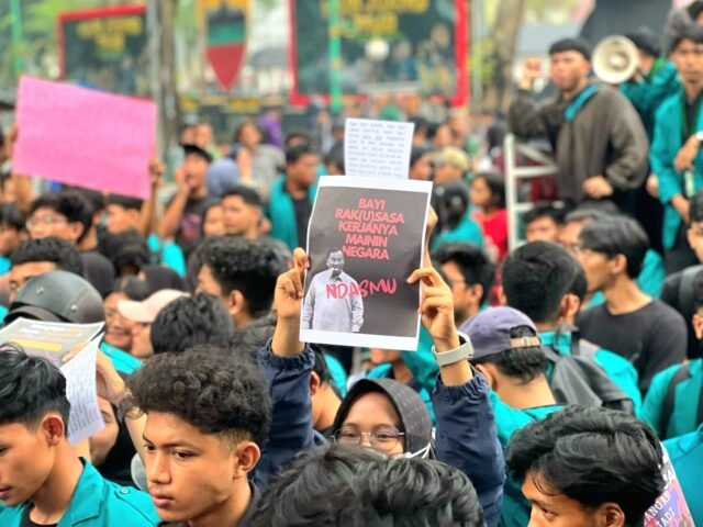 ANGKAT TINGGI | Seorang mahasiswi mengangkat poster bertuliskan "BAYI RAK(U)SASA KERJANYA MAININ NEGARA", Jumat (21/02/2025). | Jeremia Rafael Simamora