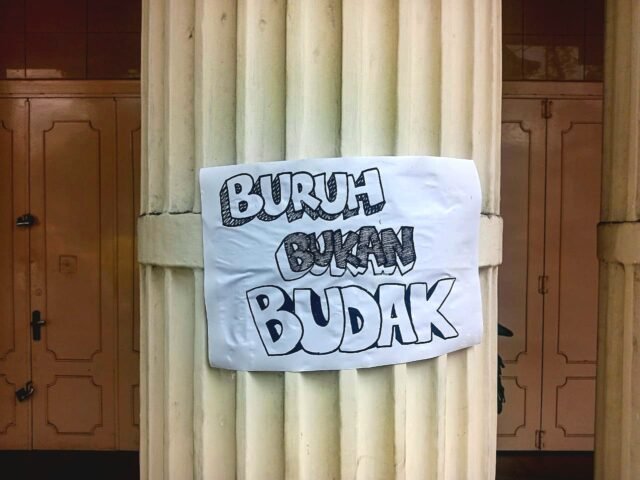 RENTETAN PROTES | Massa aksi juga menempelkan poster di sepanjang bangunan yang dilewati. Terlihat salah satu poster bertuliskan "Buruh Bukan Budak" ditempel selama aksi berlangsung, Kamis (01/05/2025). | Lody C. I. Siringo-ringo