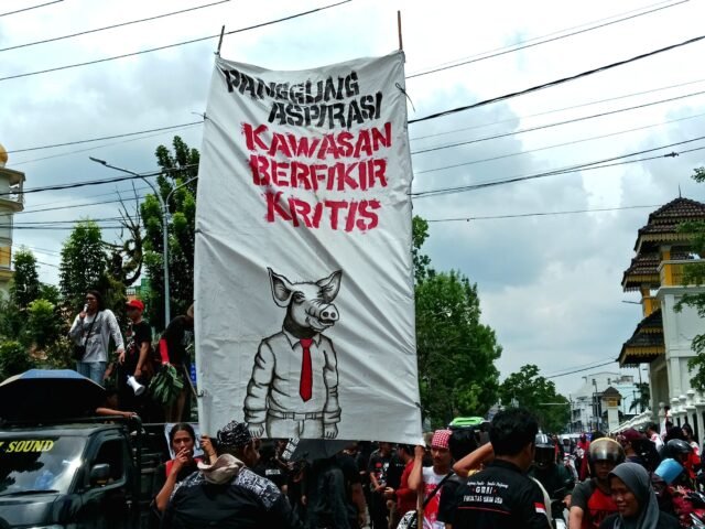 SUARAKAN | Massa aksi mengangkat spanduk besar bertuliskan “Panggung Aspirasi — Kawasan Berpikir Kritis” dengan ilustrasi babi berdasi. Sebuah spanduk sarkastik untuk membakar semangat perjuangan, (01/05/2025). | Ruth Cinthia Sianturi