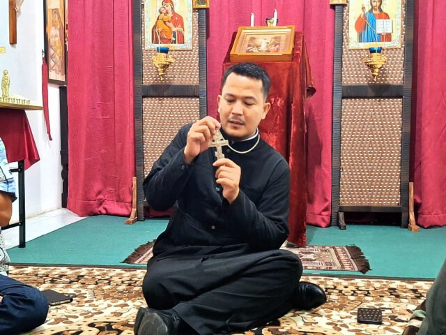 Romo Nikola menunjukkan salib Ortodoks dengan bentuk khas tiga palang, yang masing-masing memiliki makna berbeda, Minggu (27/4/2025). | Derista Putri