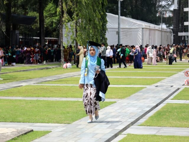 LANGKAH | Seorang wisudawati melangkah anggun dengan kebaya biru. Ia menyampirkan toga di lengan sambil menghampiri keluarganya, Jumat (29/8/2025). | Dinar Fazira Fitri