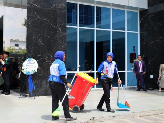 KEWAJIBAN | Dua petugas kebersihan menjalankan tugasnya di tengah suasana wisuda. Mereka sosok penting yang menjaga kenyamanan acara, Jumat (29/8/2025). | Imelda Sari Manalu