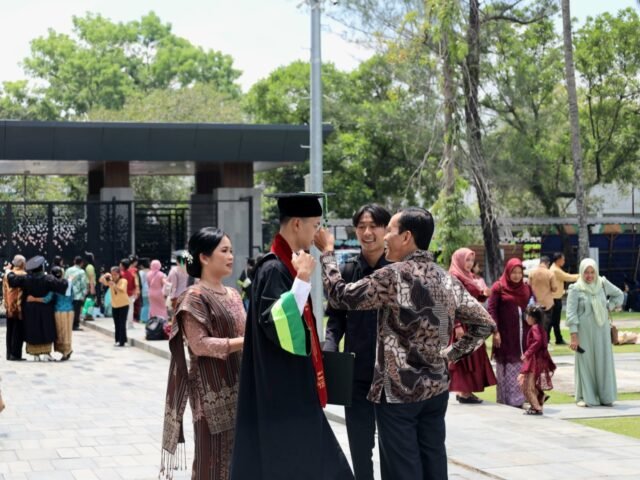 BANGGA | Seorang ayah merapikan toga anaknya sebelum berfoto bersama. Tindakan kecil sebagai simbol dukungan dan rasa bangga keluarga di hari wisuda, Jumat (29/9/2025). | Imelda Sari Manalu