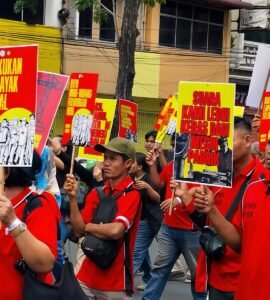 POSTER | Massa aksi tampak membawa berbagai poster bernada tuntutan dengan desain seragam berwarna merah dan kuning. Poster-poster tersebut menjadi simbol perlawanan sekaligus media penyampai aspirasi buruh di tengah aksi, Jumat (1/5/2026). | Iyusarah Pakpahan