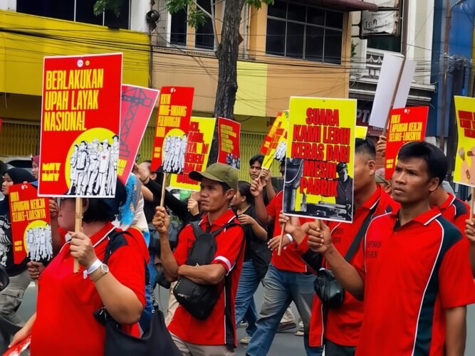 POSTER | Massa aksi tampak membawa berbagai poster bernada tuntutan dengan desain seragam berwarna merah dan kuning. Poster-poster tersebut menjadi simbol perlawanan sekaligus media penyampai aspirasi buruh di tengah aksi, Jumat (1/5/2026). | Iyusarah Pakpahan