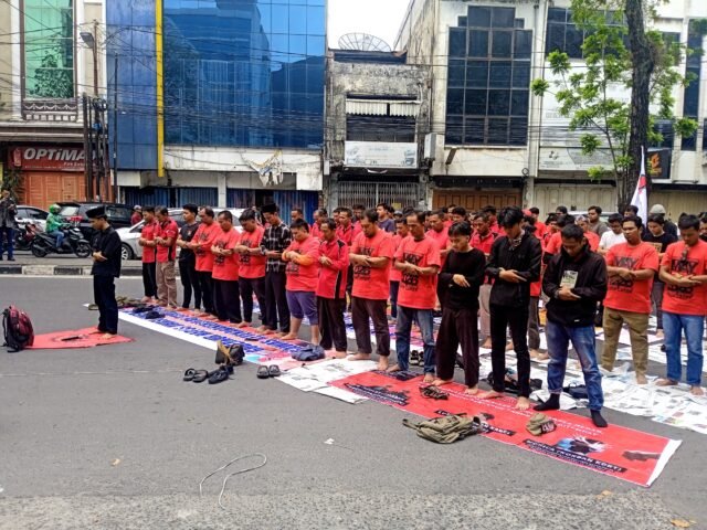 SEJENAK | Sejumlah massa aksi melakukan ibadah Salat Jumat beralaskan spanduk dan bendera di jalan depan Dipo Star Finance, Jumat (1/5/2026). | Jennifer Smith L. Tobing
