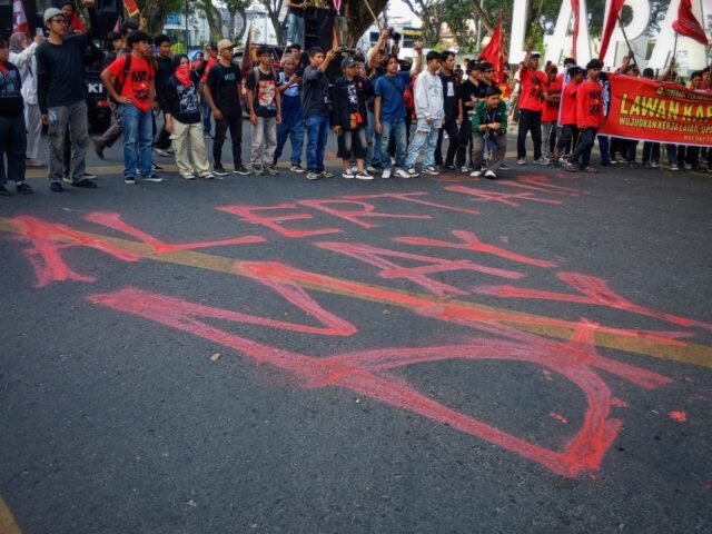 TERPAMPANG | Tampak tulisan “ALERTA!! MAY DAY” di badan jalan sebagai simbol penyampaian aspirasi massa dalam aksi Hari Buruh di depan Lapangan Merdeka. Aksi berlangsung tanpa kehadiran perwakilan pemerintah, Jumat (1/5/2026). |Jessica Fransiska Br Tarigan